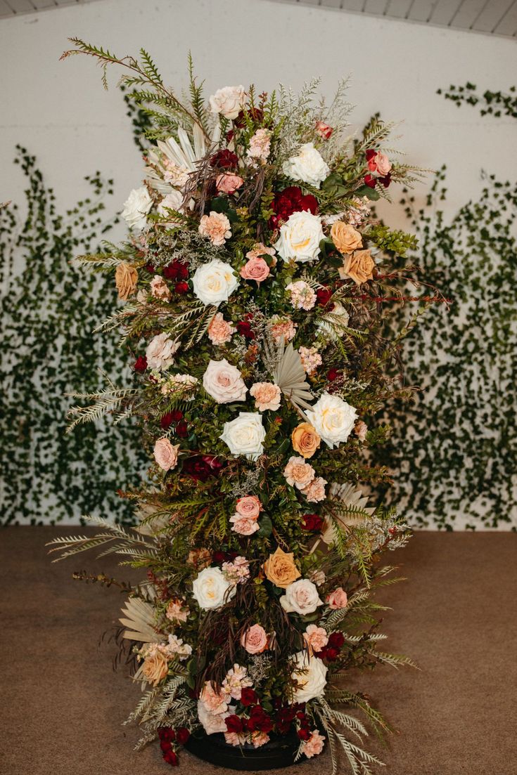 an arrangement of flowers in a vase on the floor next to a wall with greenery