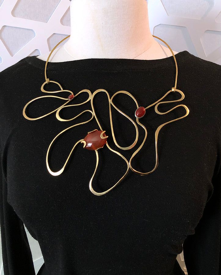 A bold contemporary sculpture to wear. This statement necklace is made for the person who likes to stand out in a crowd. It is a unique piece that you’ll reach for every time you want to be noticed. Hand-shaped and hammered brass wire with three carnelian stones. It has been lacquered to slow oxidation. The centerpiece is 81/2 inches across by 5 inches tall. It closes with hook and eye. It is 20 inches long and is shown on a size 12 dress form. Contemporary Handmade Necklace, Unique Freeform Gold Necklace, Modern Brass Necklace, Brass Jewelry Design, Hammered Metal Jewelry, Aluminum Wire Jewelry, Contemporary Jewellery Necklace, Metal Art Jewelry, African Beads Necklace