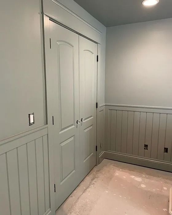 an empty room with white walls and gray paneling on the wall, two doors are open