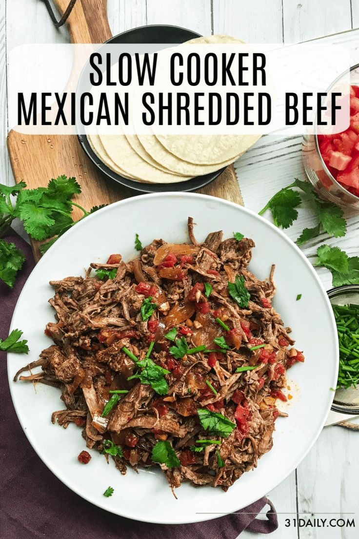 slow cooker mexican shredded beef on a white plate with tomatoes and cilantro