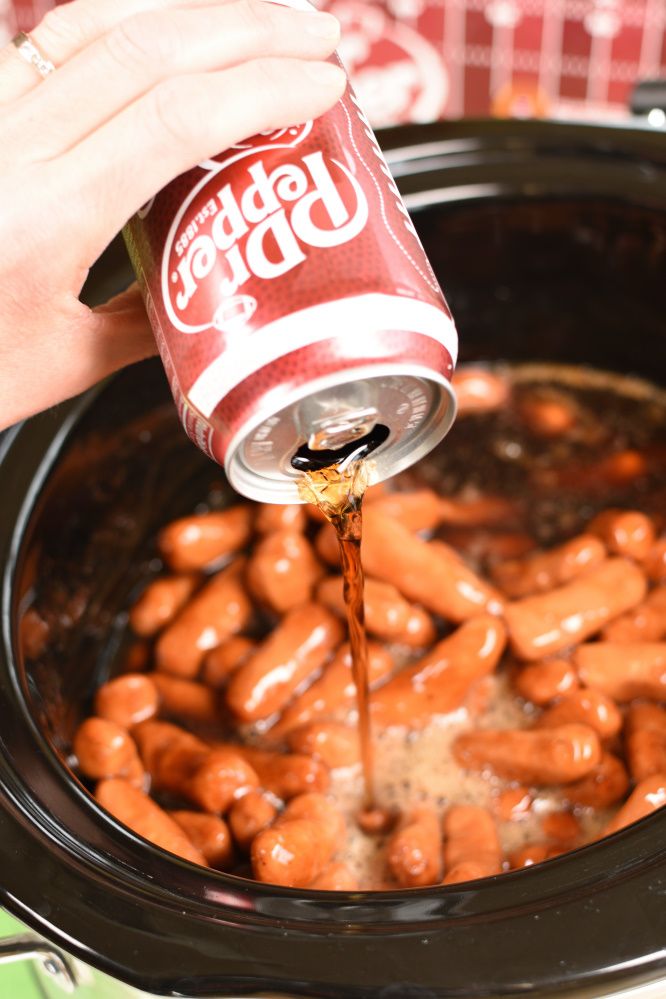 a person pouring soda into a crock pot filled with hot dogs