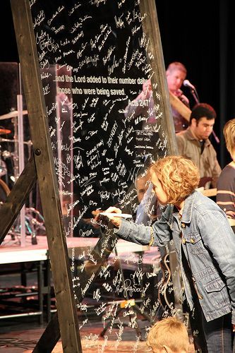 a woman writing on a glass wall with people in the background at a stage setting