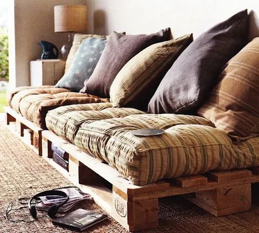 a couch made out of wooden pallets with pillows on it and headphones laying on the floor