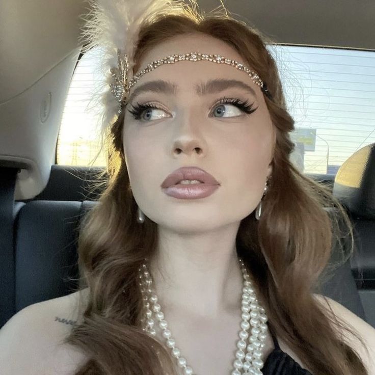 a woman with long hair wearing pearls and a tiara in the back seat of a car