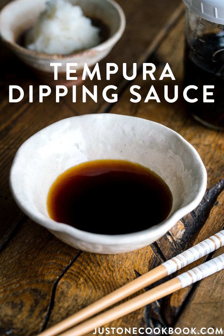 there are chopsticks next to a bowl of dipping sauce on the wooden table