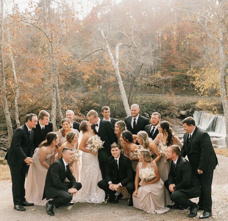 a large group of people standing next to each other in front of a waterfall and trees