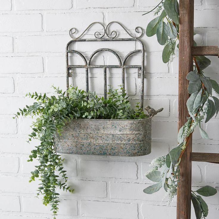 a metal planter hanging from a brick wall next to a ladder with greenery in it