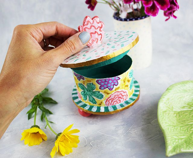 a hand is holding a small box with flowers in it next to some other items