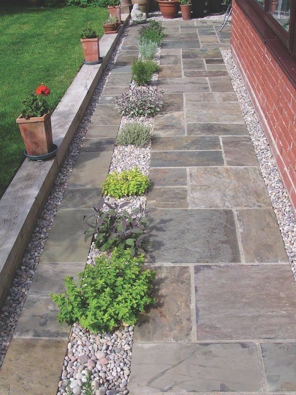 a stone walkway in front of a brick building with potted plants on the side