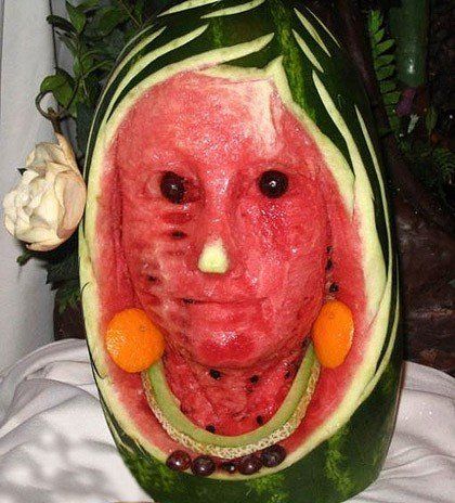 a watermelon carved to look like a man's face with fruit around it