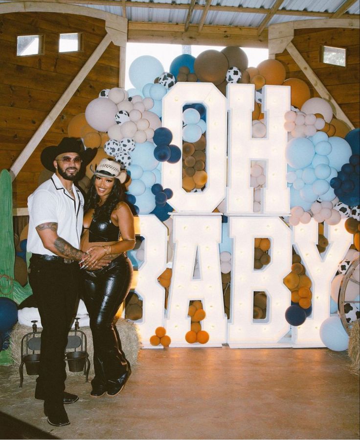 a man and woman standing next to each other in front of balloons that spell out oh baby