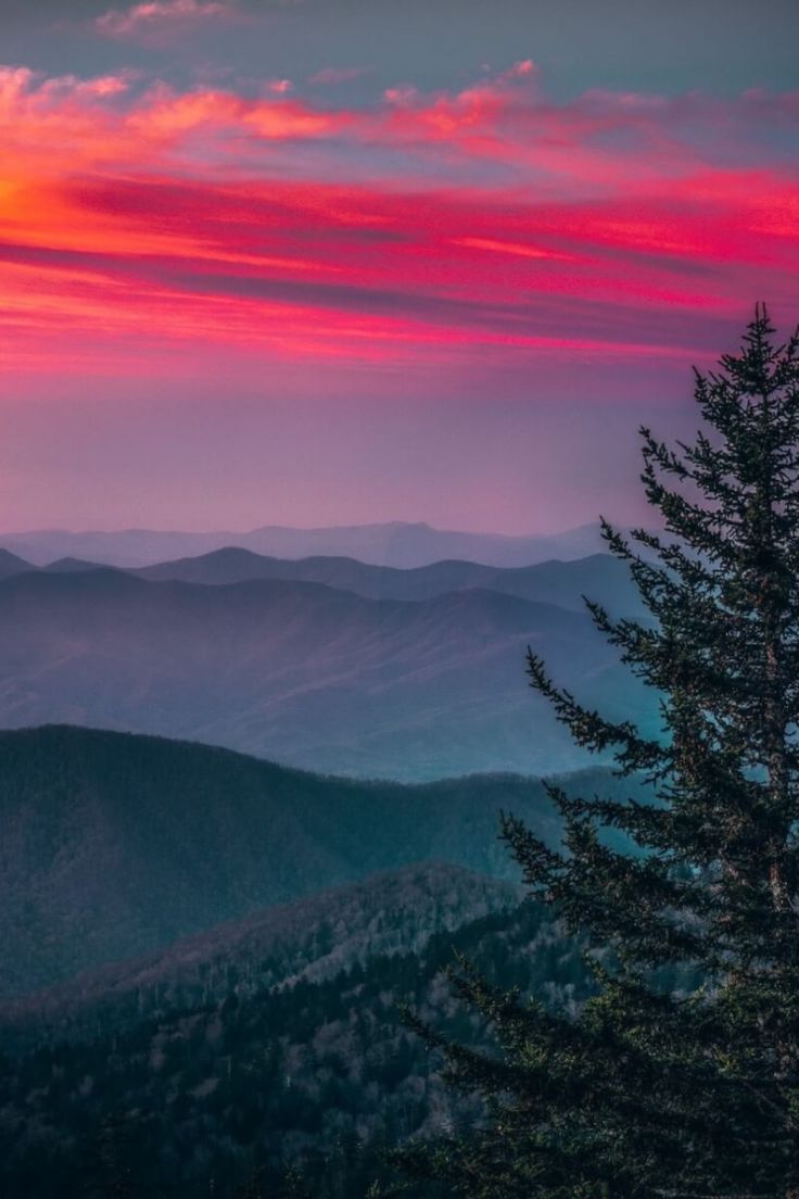 the sun is setting over mountains with trees in the foreground and clouds in the background