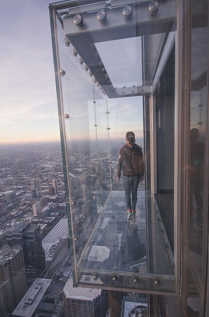 a man standing on top of a tall glass structure in the middle of a city