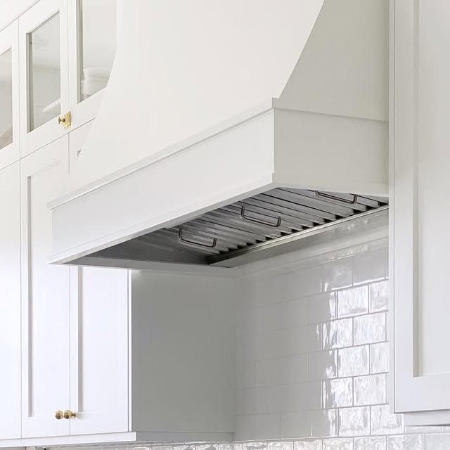 a kitchen with white cabinets and an oven hood over the stove top in front of some cupboards