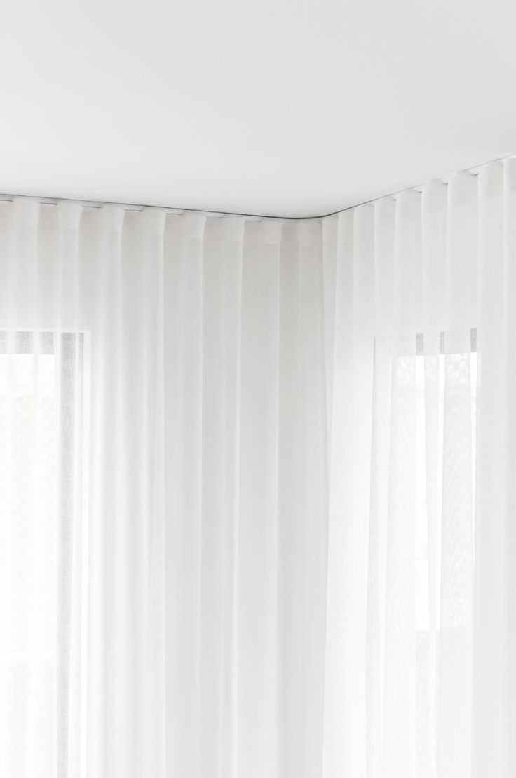 a bed sitting under a window next to a white curtained wall in a bedroom