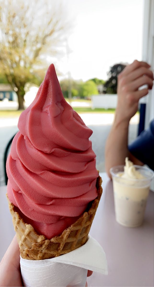 a person holding up an ice cream cone with pink icing on it's top