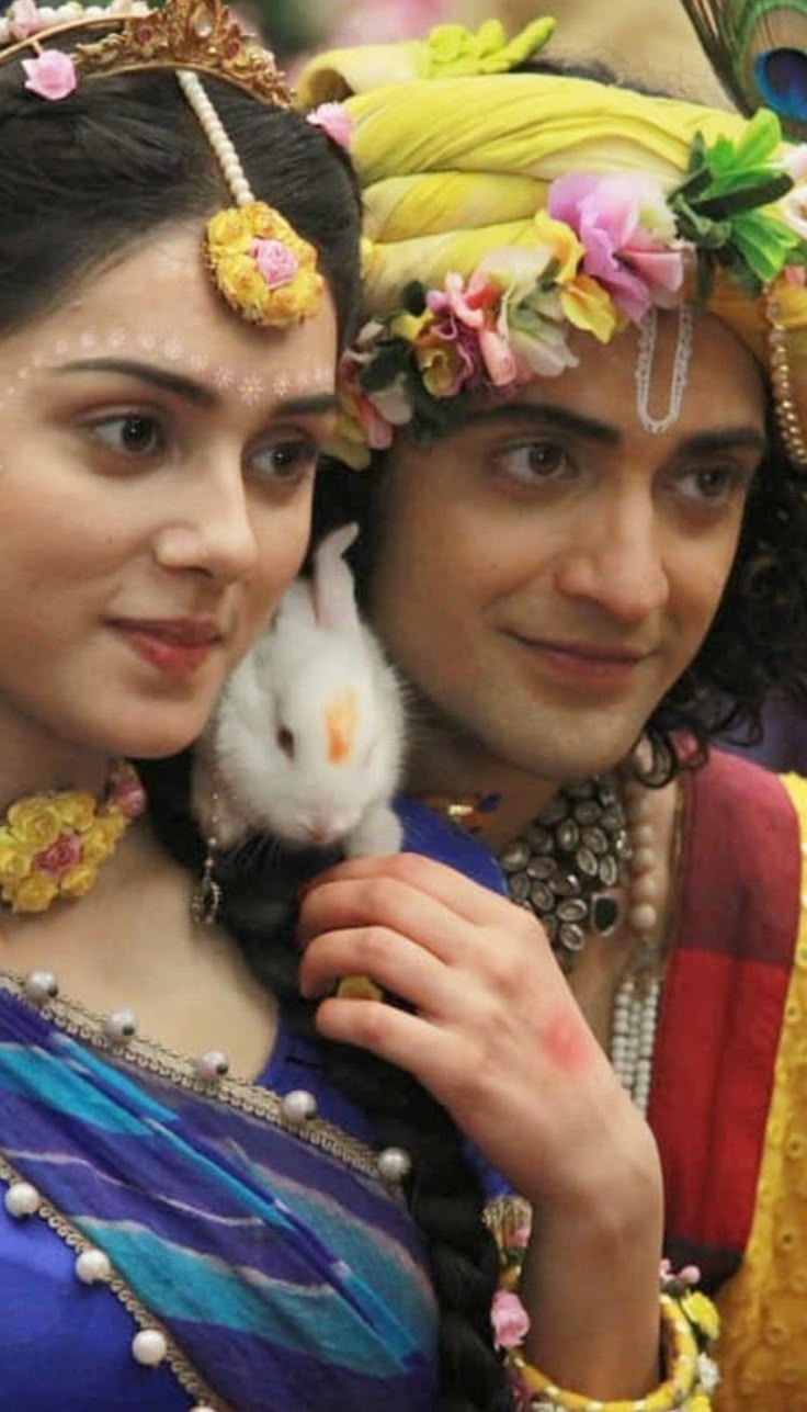 a man and woman dressed in costume holding a small white animal while standing next to each other