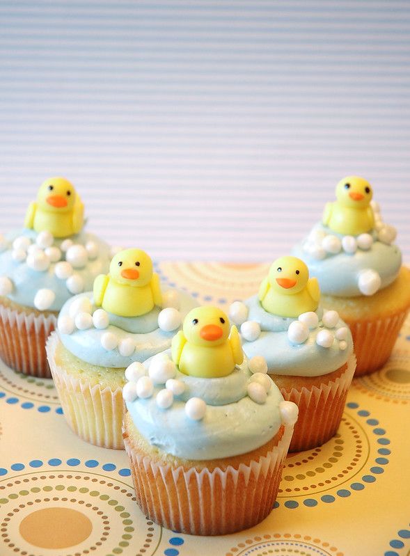 four cupcakes with yellow rubber ducks on them sitting on a tablecloth covered surface