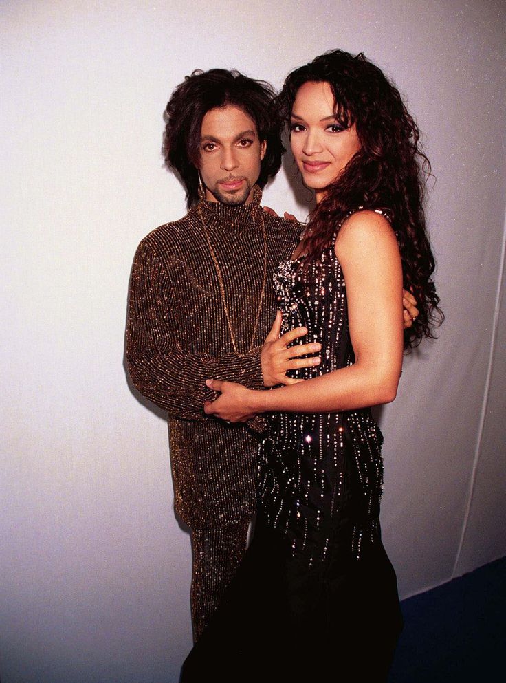 a man and woman standing next to each other in front of a white wall with an advertisement on it