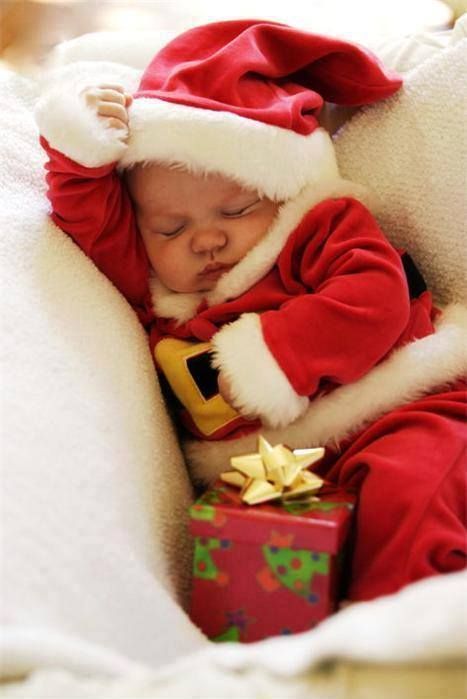 a baby in a santa suit sleeping next to a christmas present