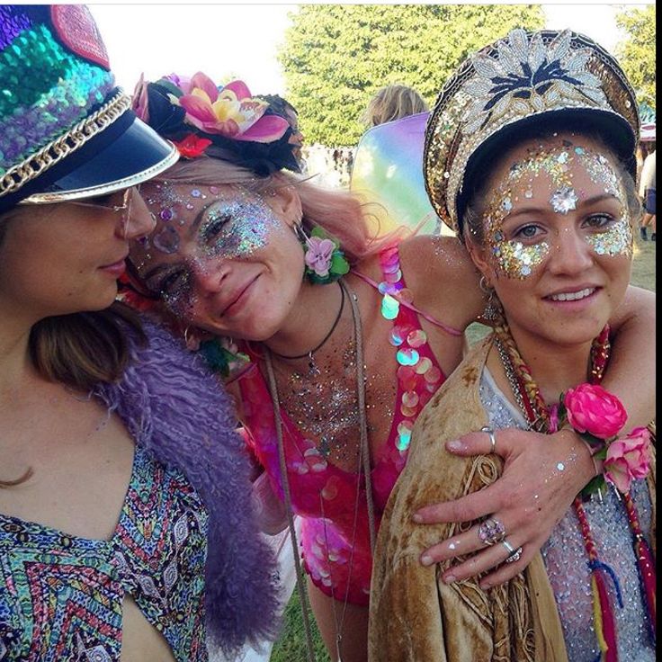 three women with their faces covered in glitters and hats at an outdoor event together