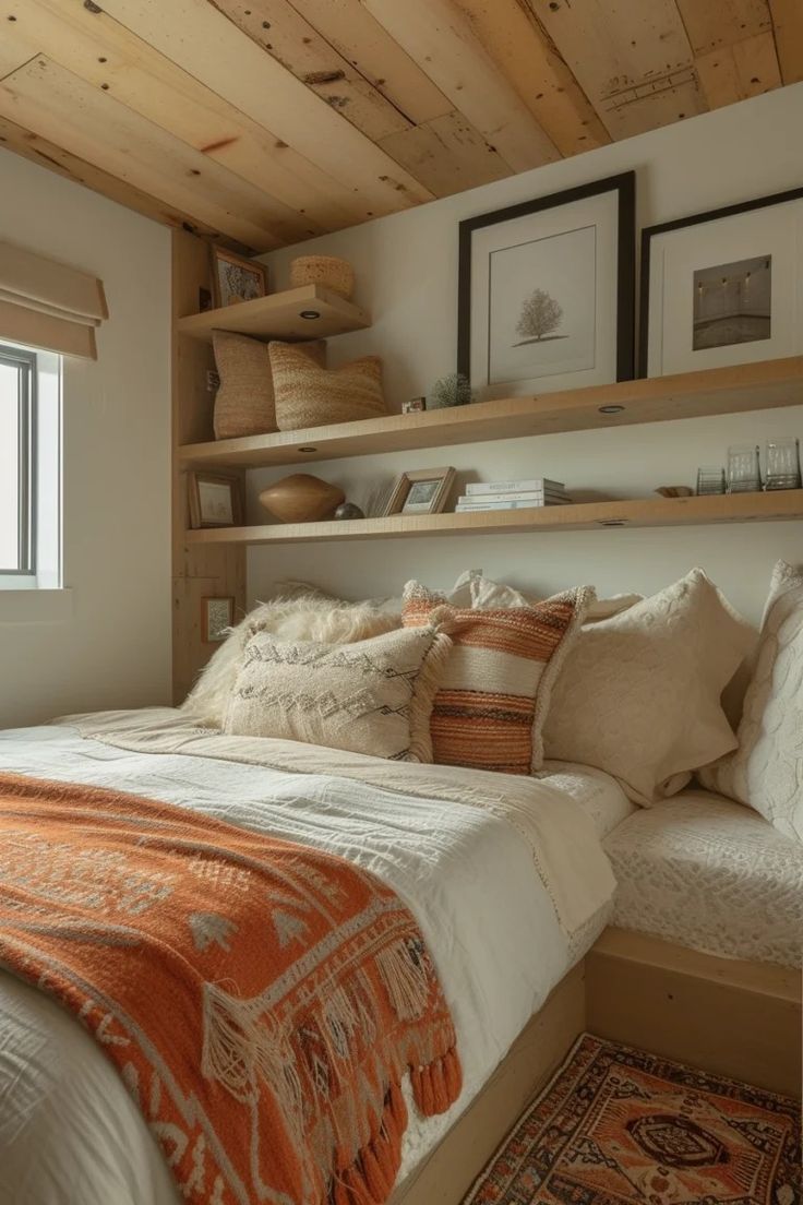 a bed sitting under a window next to a wooden shelf filled with pillows and blankets