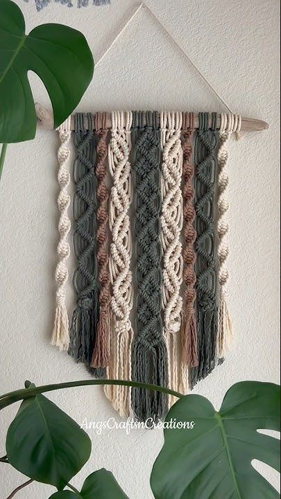 the wall hanging is made up of different colored yarns and tassels, along with a green plant