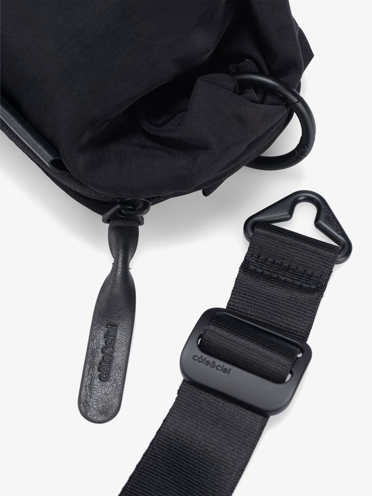 Made from a nylon fabric, the NESTOS is a compact pouch fitted with a carry strap. Featuring a main compartment with zipper access, it offers ample storage for those on the go. Matte black hardware with côte&ciel engraving allow the NESTOS to be worn as a crossbody on its own, as well as to be docked onto other pieces using the circular carabiners, which are positioned in both swirls. Black Pouch, Matte Black Hardware, Nylon Fabric, Black Hardware, The Go, Matte Black, Pouch, Zipper, Fabric