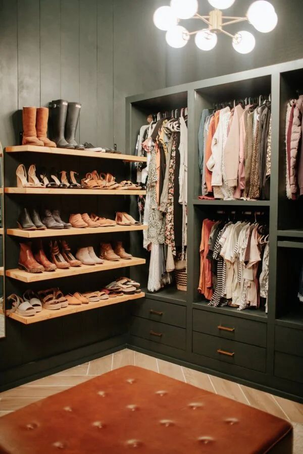 a walk in closet filled with lots of shoes and clothing hanging on wooden shelves next to a brown ottoman