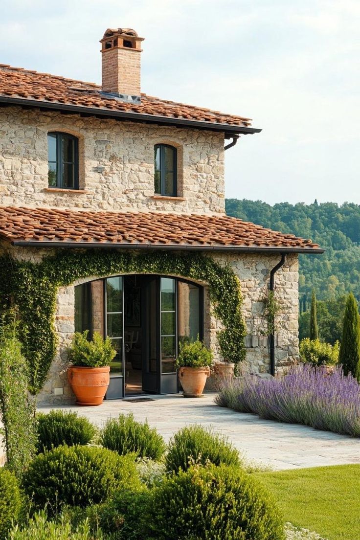 a stone house with potted plants in the front yard and an entry way leading to it