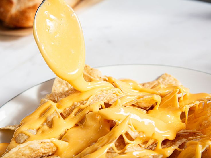 a spoon full of cheese sauce being poured over some tortilla chips on a plate