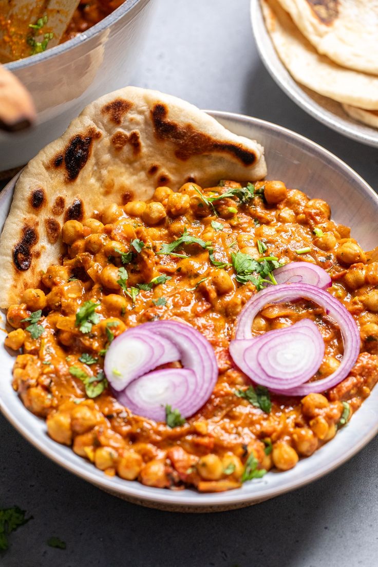 a bowl filled with chickpeas and onions next to pita bread on a table