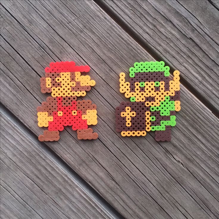 two pieces of perler bead art sitting on top of a wooden table next to each other