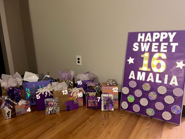 purple and white birthday gifts are on the floor next to a sign that says happy sweet 16 amalia