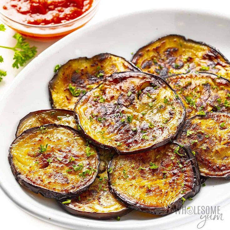 cooked eggplant slices on a white plate with ketchup and parsley