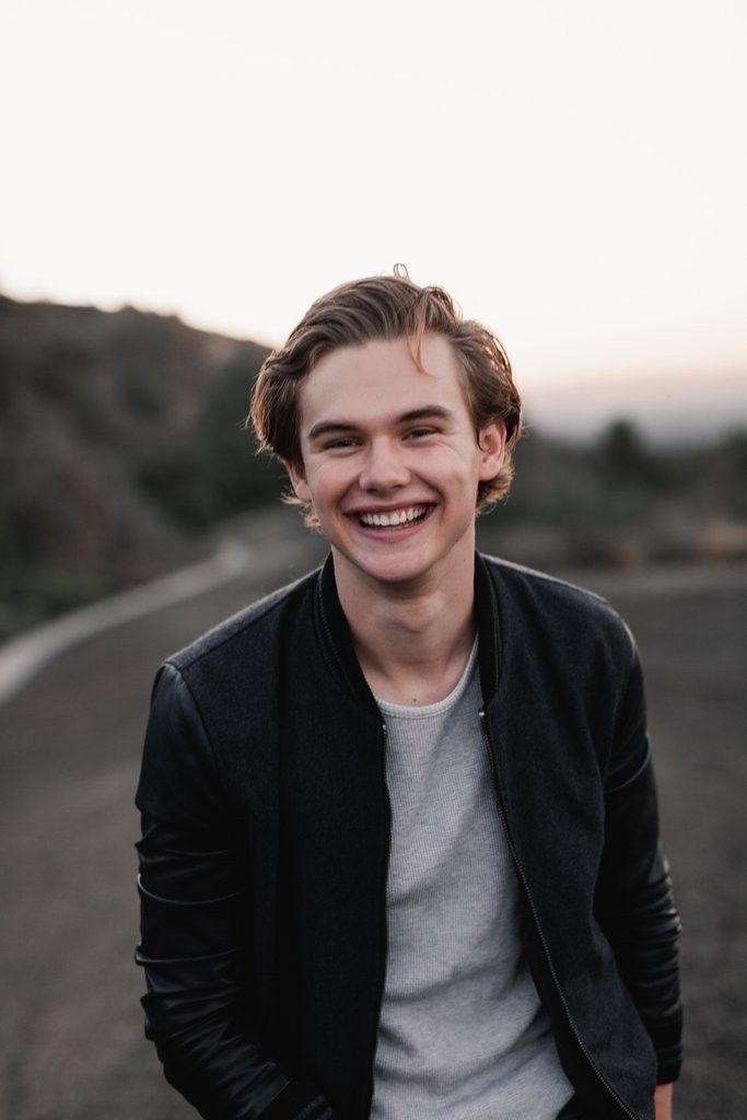 a smiling young man sitting on the side of a road