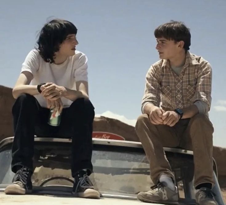 two young men sitting on the back of a pickup truck talking to each other,