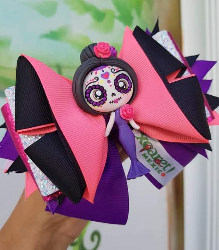 a hand holding a pink and black hair bow with a skull doll on it's head