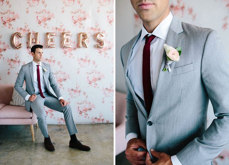 a man in a suit and tie sitting on a chair next to a wall with flowers