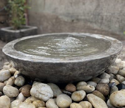 a stone bowl is sitting on top of some rocks and pebbles, with water coming out of it