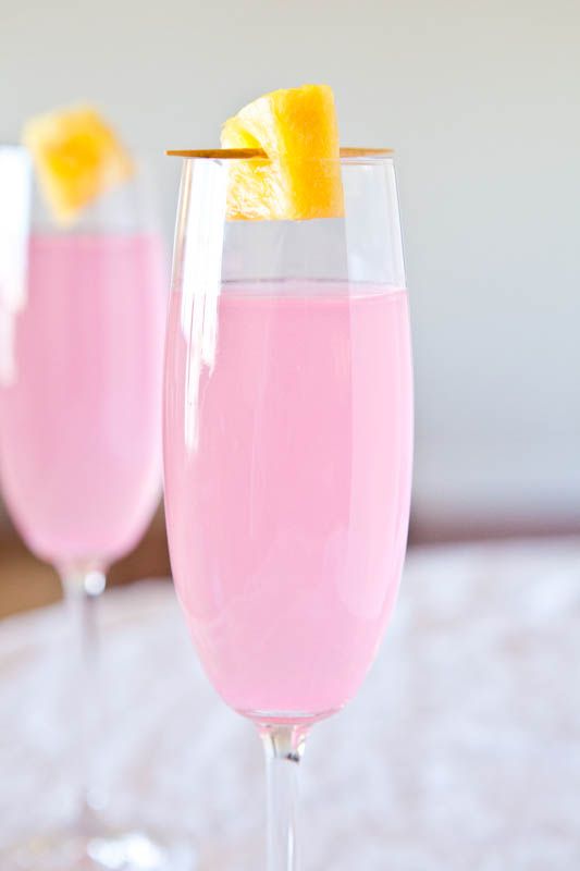 two wine glasses filled with pink liquid and orange wedges on the rim, sitting on a table