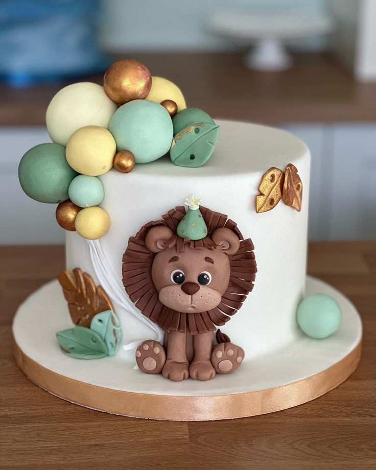 a white cake with a lion on top and balloons around the edges, sitting on a wooden table