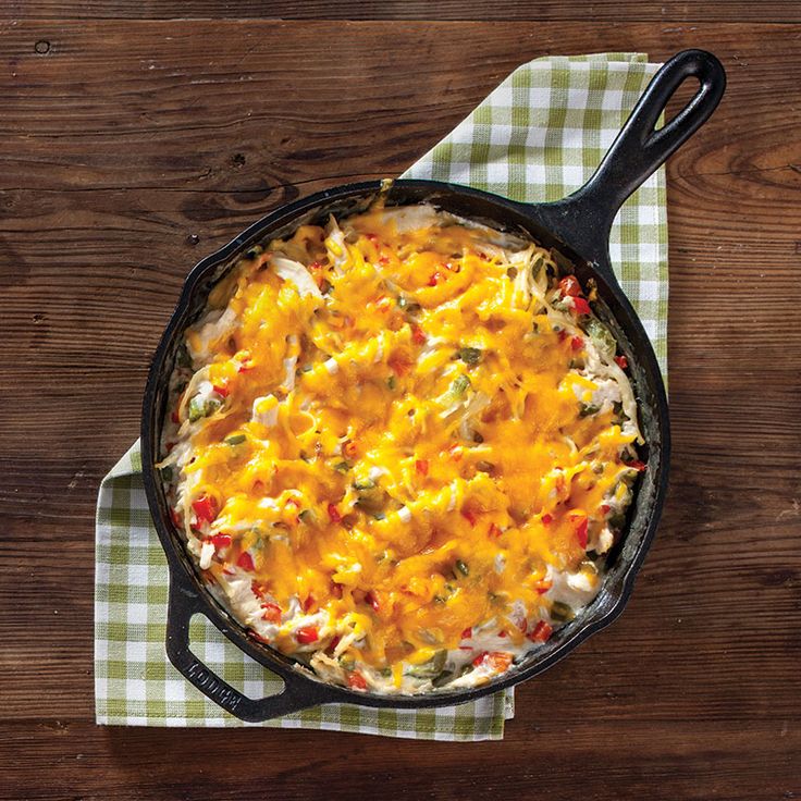 a skillet filled with cheese and vegetables on top of a green checkered napkin