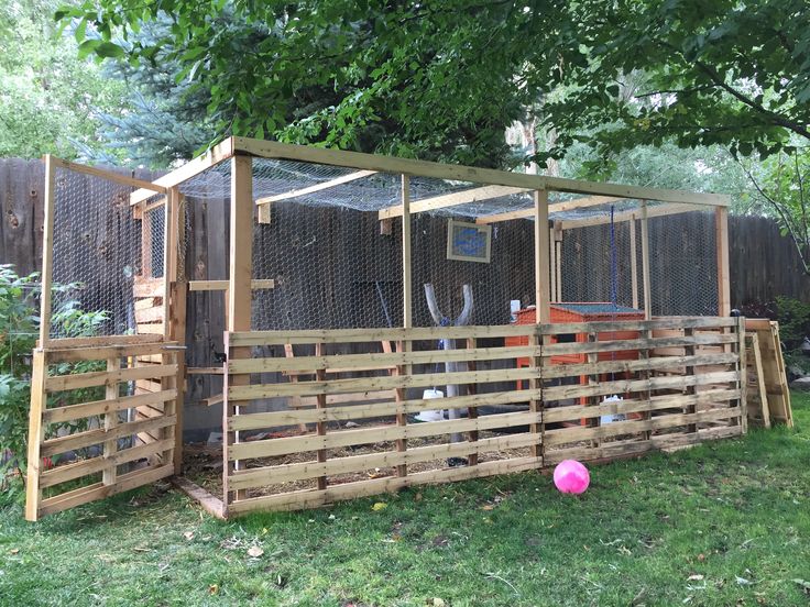 a chicken coop built into the side of a fenced in area with a pink ball