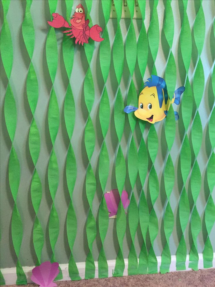 some paper fish are hanging on the wall in front of green wavy lines and pink flowers