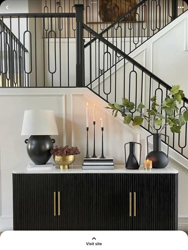 a black and gold sideboard with vases on it in front of a staircase