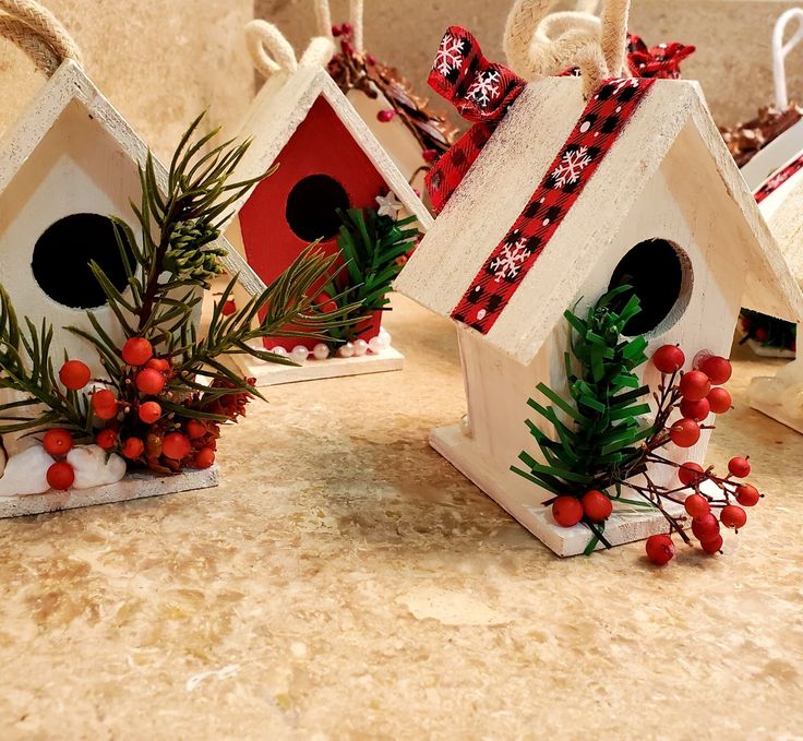 three birdhouses decorated with red berries, pine cones and bows on top of a counter