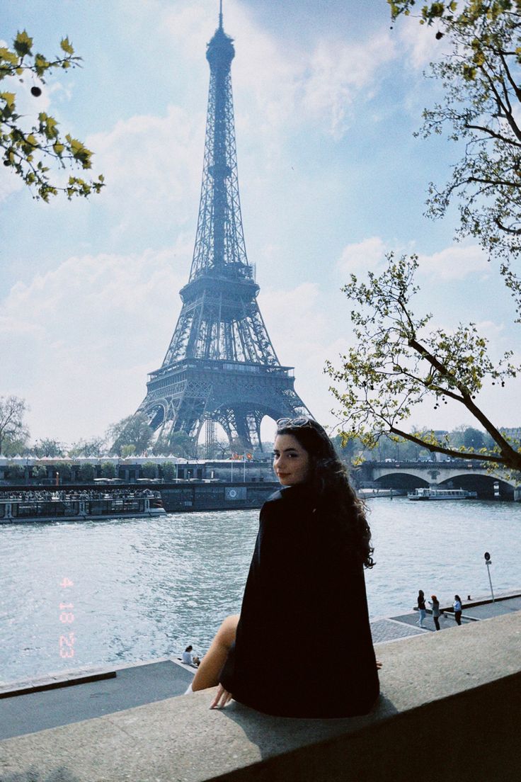 a woman sitting on a ledge in front of the eiffel tower