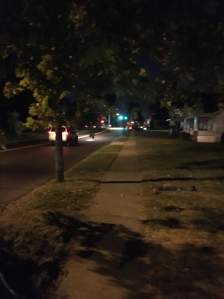 a street at night with cars parked on the side and trees in the foreground