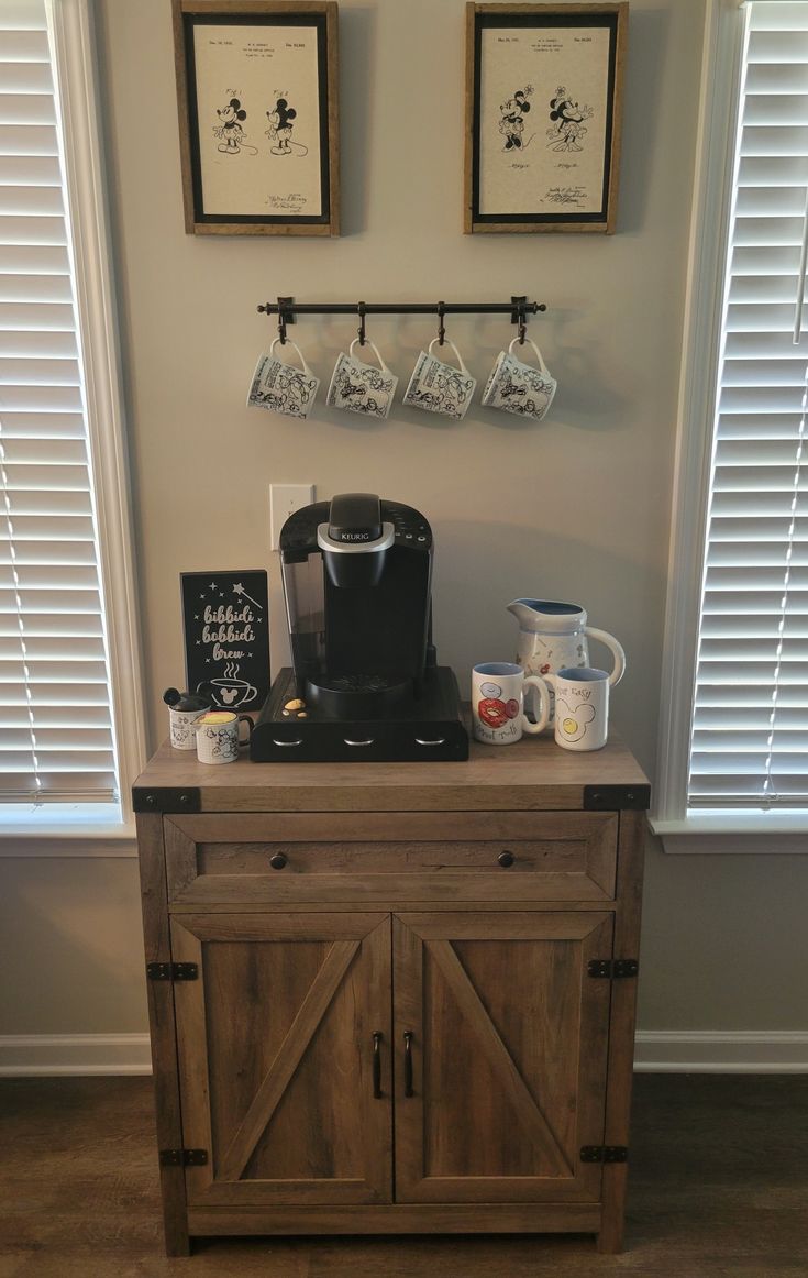 a coffee maker on top of a wooden cabinet in front of two framed pictures above it